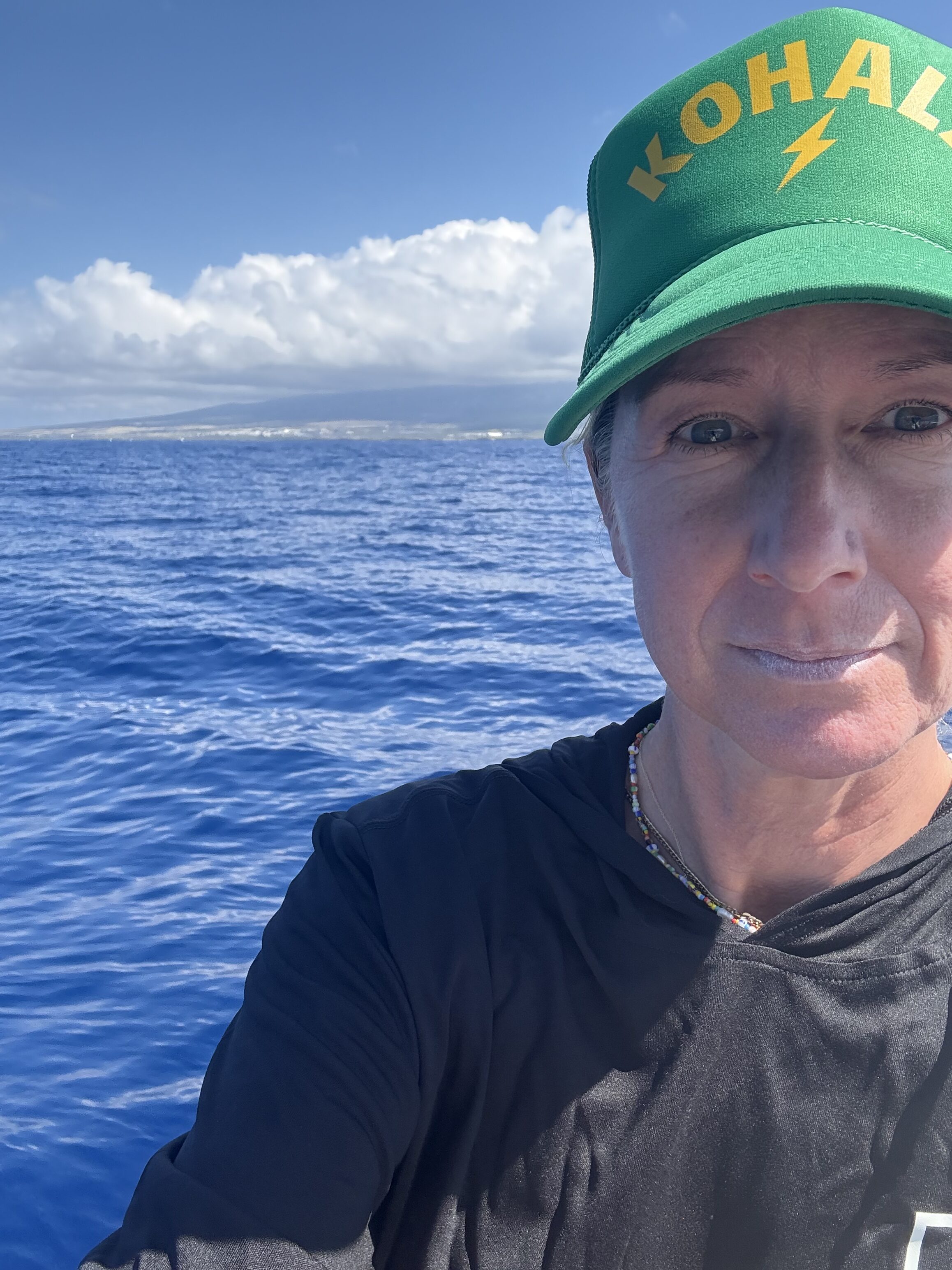 Woman in black shirt with green hat with the ocean and blue sky background